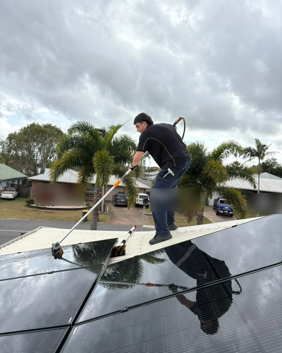 Next Phase Solar crew member cleaning a rooftop solar array with a water-fed pole
